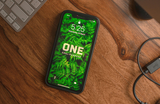 An eco-friendly iPhone cover on a wooden table besides a cord and keypad.