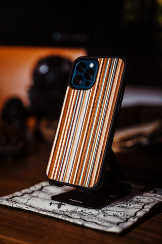 A smartphone with a striped wooden phone case is placed upright on a stand over a vintage-style map cloth on a wooden desk.