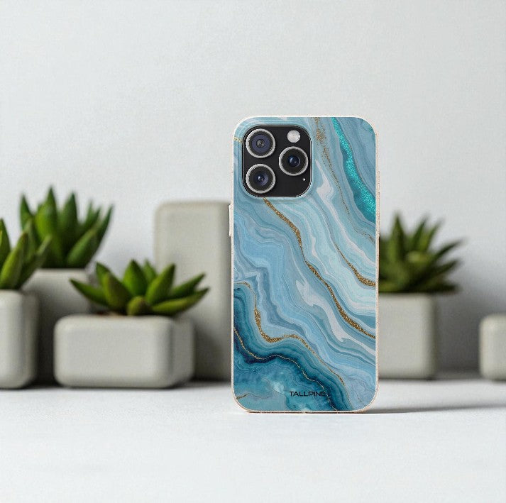 Phone case with blue and gold marble pattern on a white surface with plants in the background