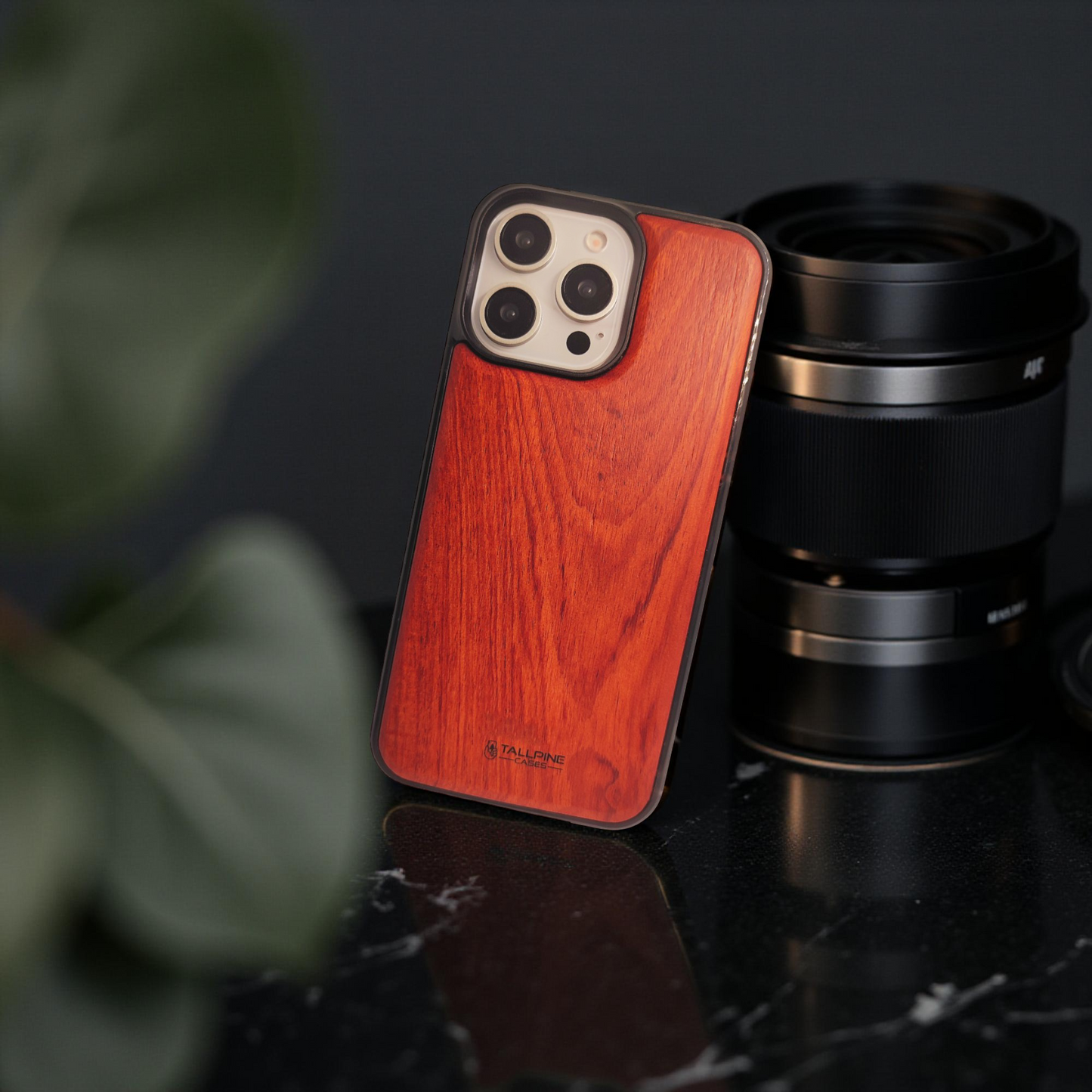 Phone case with wooden texture next to camera lens on a dark surface