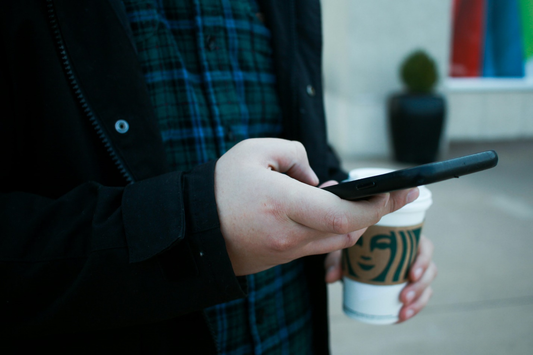 person holding s phone and a coffee 